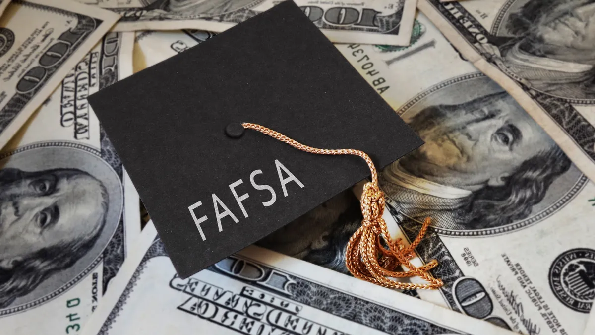 Dollar bills are scattered. On top of the bills is a small gradulation cap with the words "FAFSA."