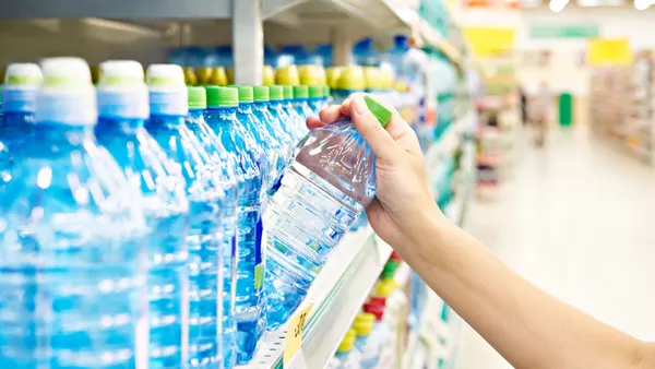hand pulls plastic beverage bottle off of store shelf lined with bottles