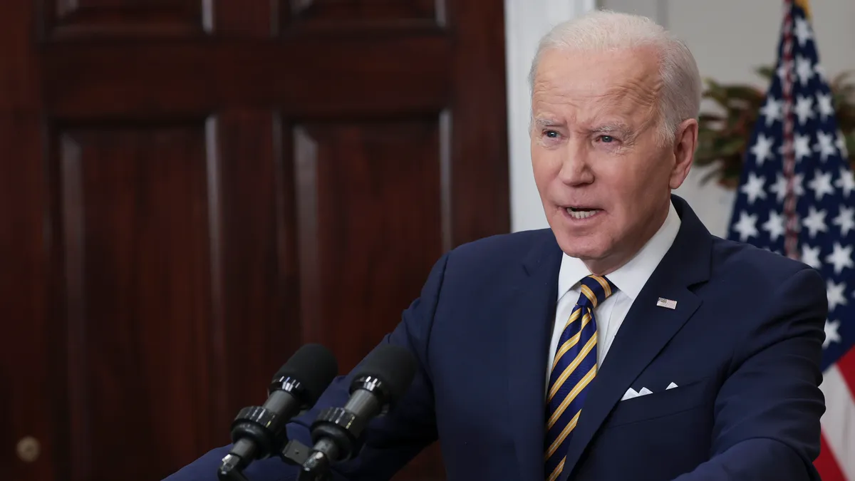 Biden stands behind a podium wearing a navy suit.