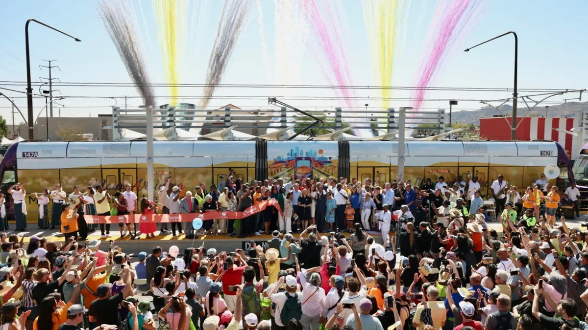 A crowd is gathered in front of a shiny train in Phoenix, with colorful smoke in the background.