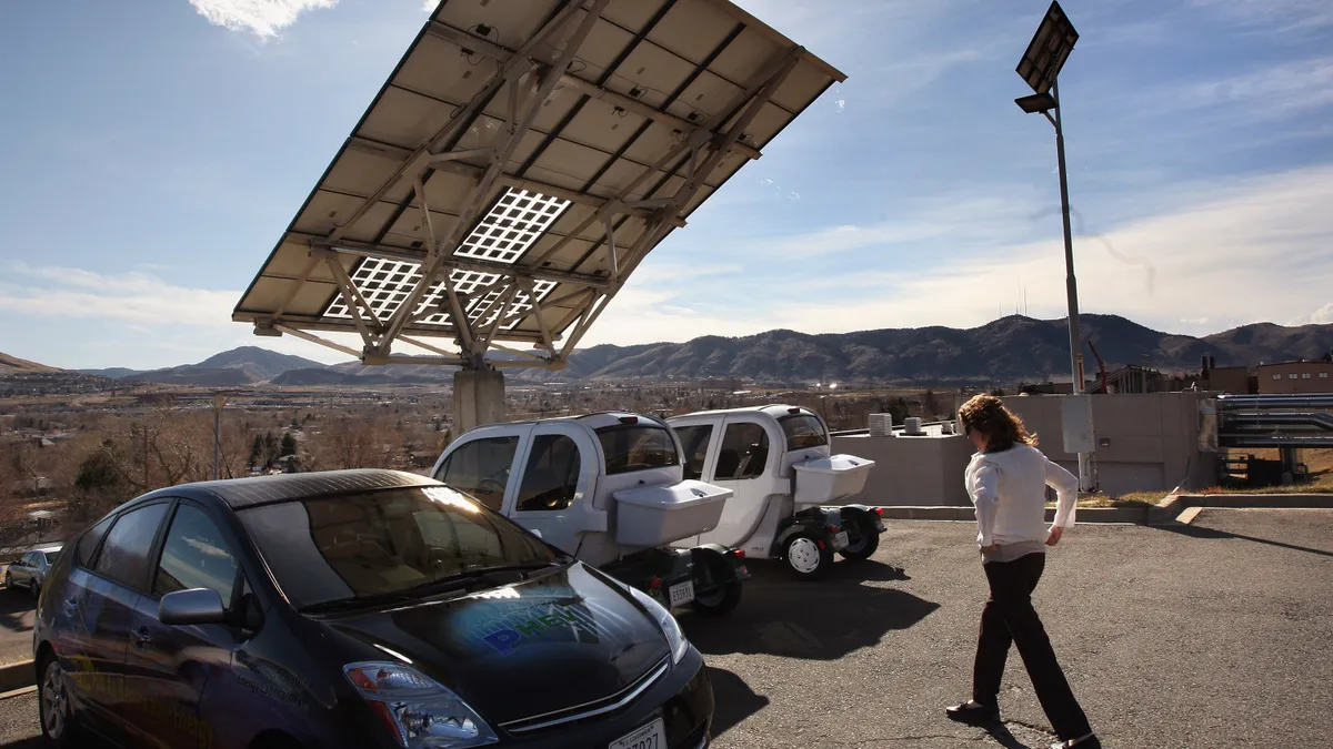 Electric vehicles charge under a solar panel.