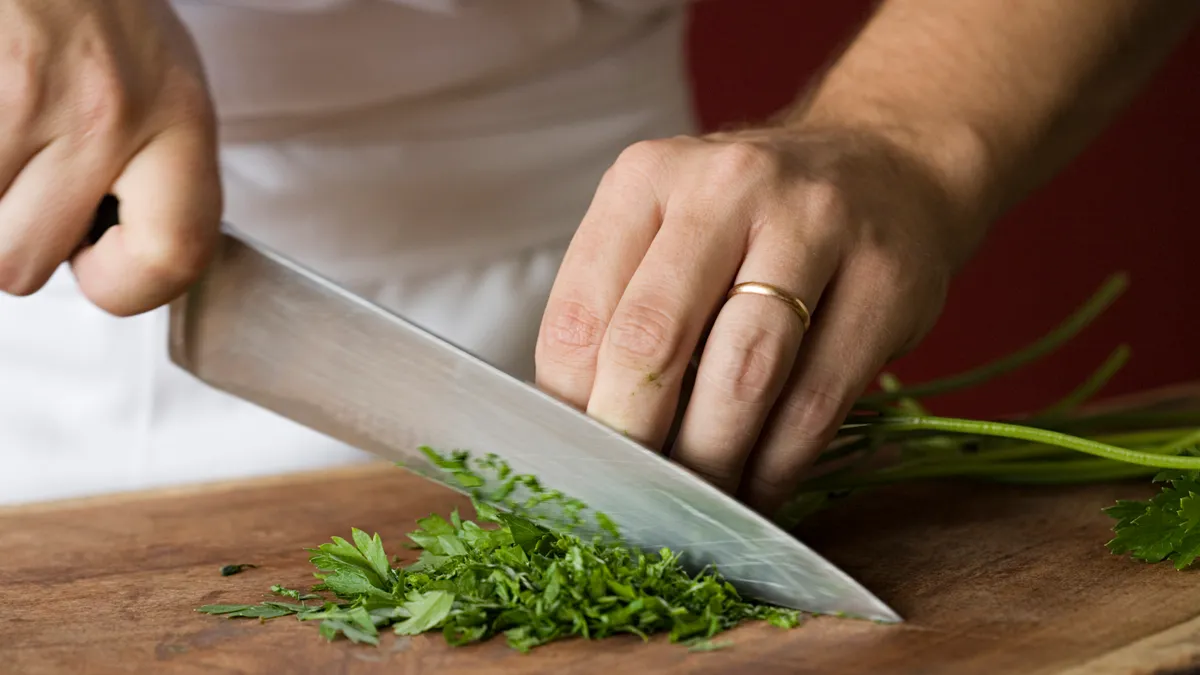 A chef chopping parsley with a knife.