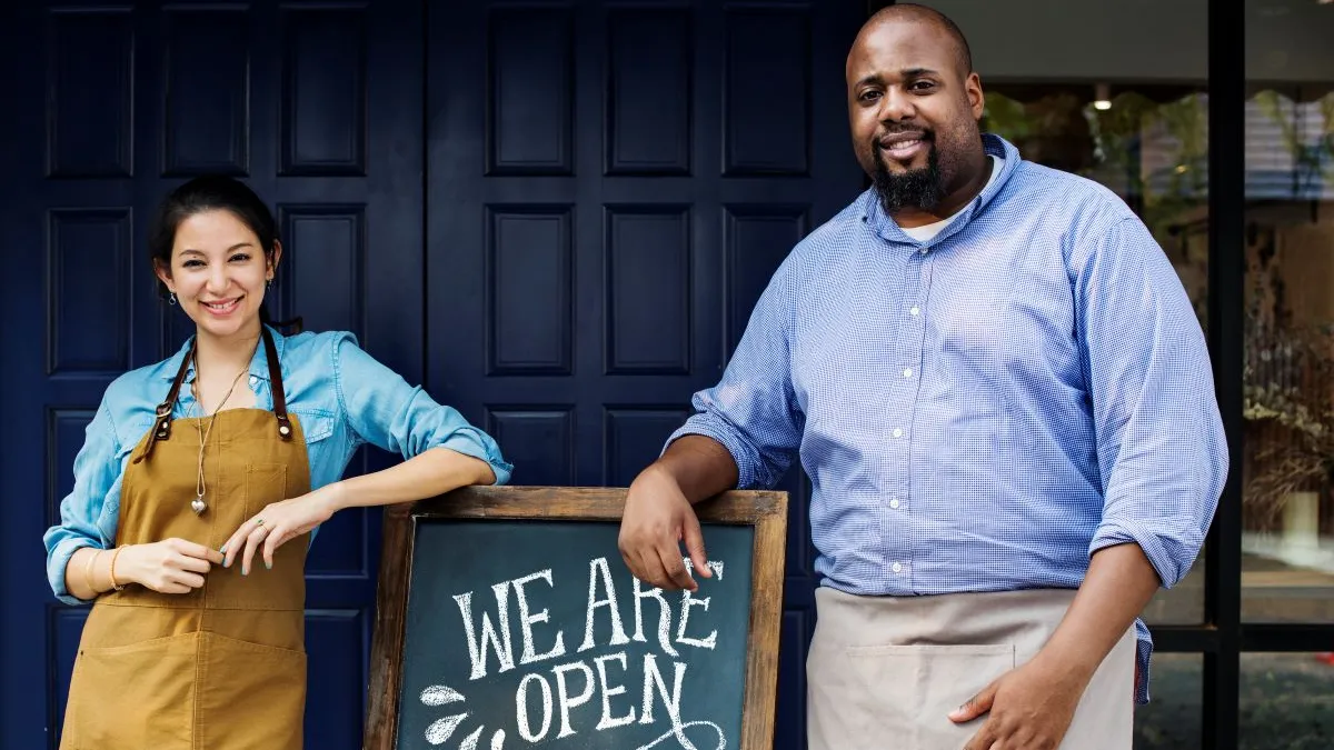 An image of a woman and a man standing next to a calkboard sign that says "we are open for brunch lunch dinner."