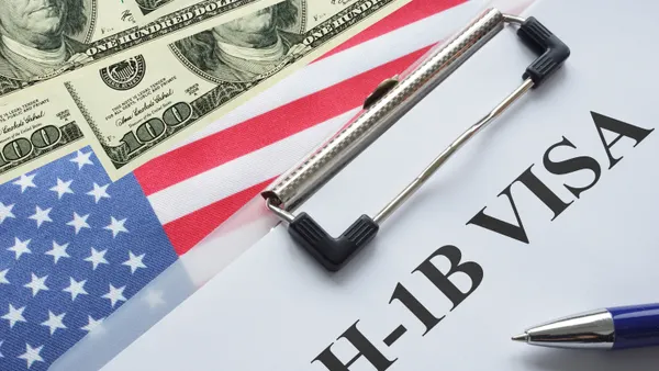 White clipboard with H1B visa written on it with a hundred dollar nearby