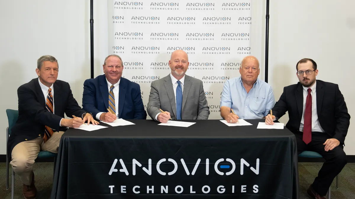 Four men sitting at a table with a black table cloth over with "Anovion Technologies" in white font.