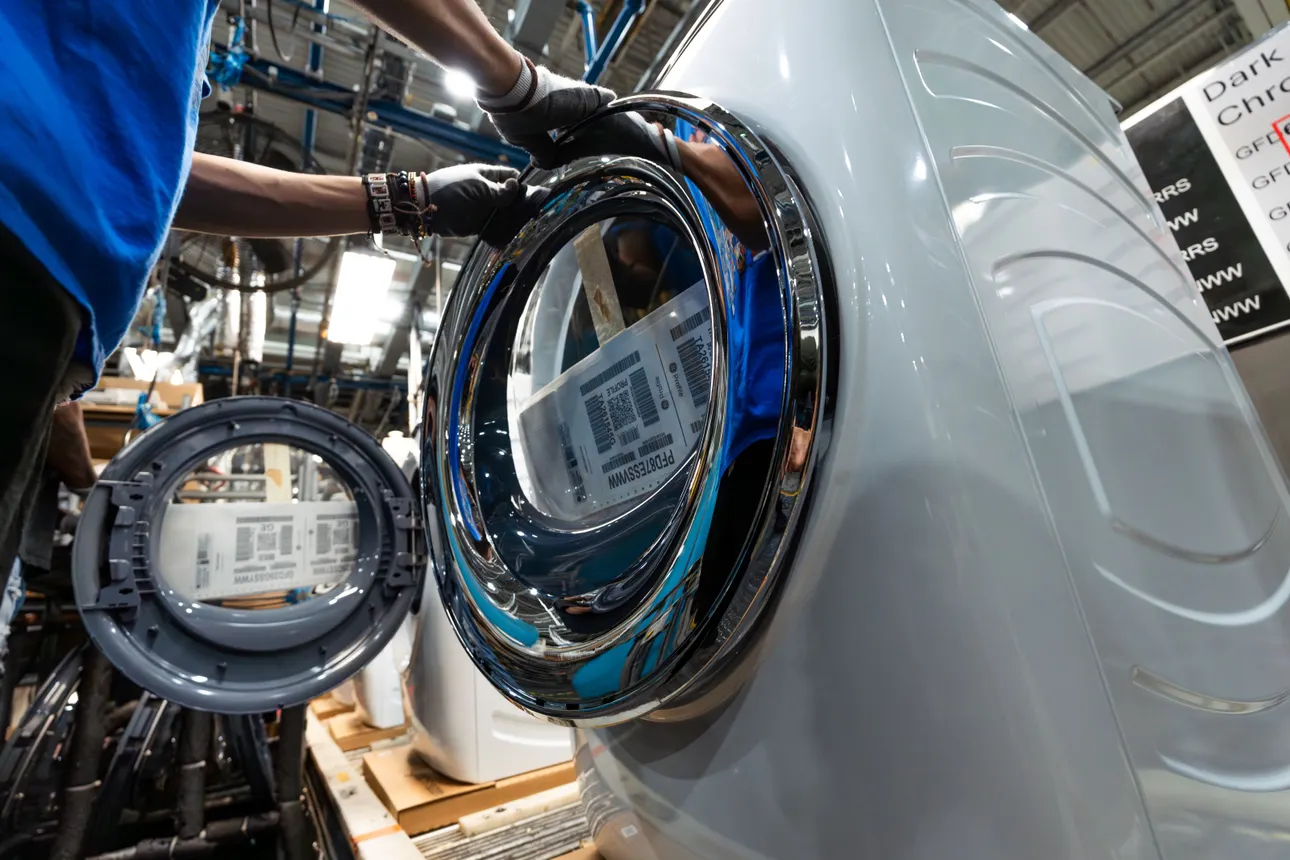 A worker attaches a component onto a laundry machine.