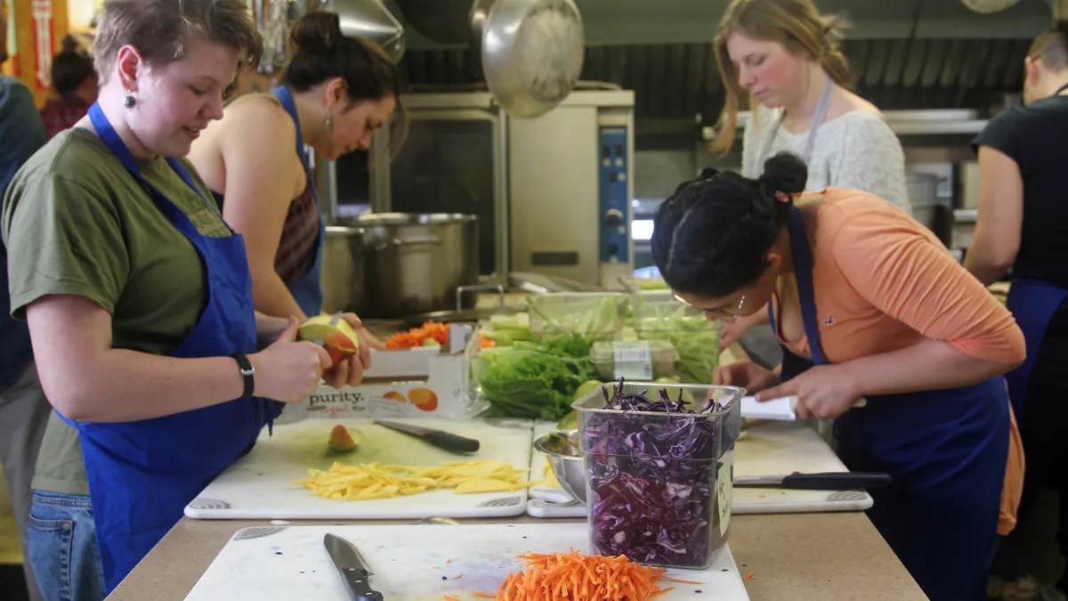 Four young women participate in a cooking class in an industrial kitchen.