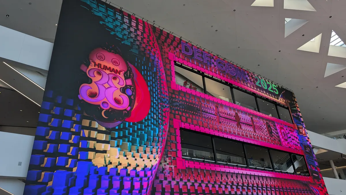 A massive electronic screen that says "DEF CON 2025" and "HUMAN 33" hangs in a large atrium.