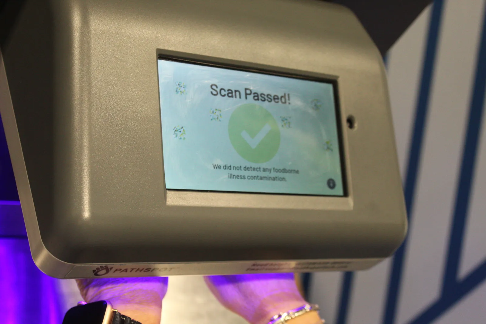 A woman scans her hands under Pathspot's contaminant scanner.