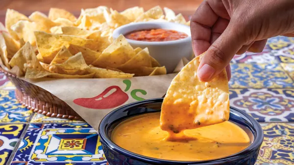 A person dips a chip in Chili's queso