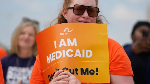 Person holding a yellow sign that says "I AM MEDICAID, Don't Cut Me!"