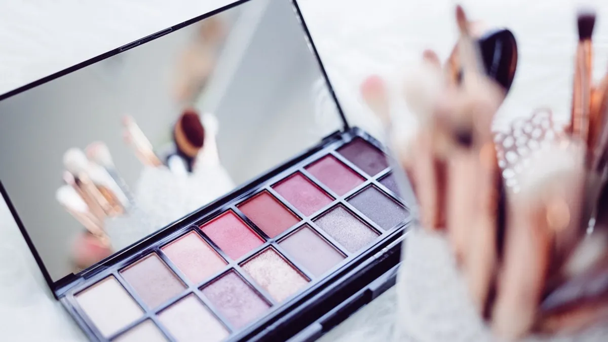 Eyeshadow pallet with a mirror sits on a table, with slightly out of focus makeup brushes.