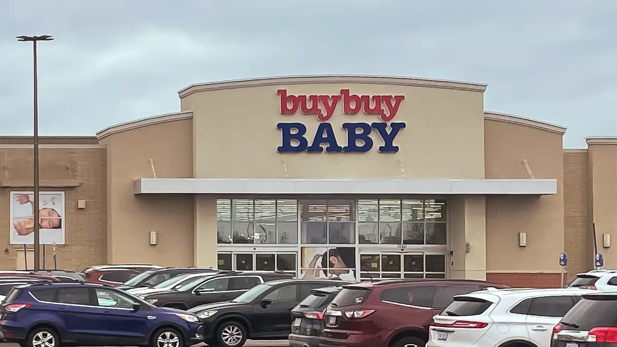 Several cars parked in a lot in front of a "BuyBuy Baby" store.