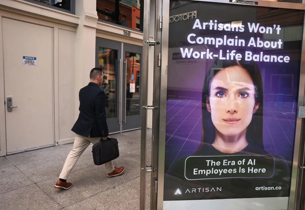 A man with a suitcase walks past an advertisement for artificial intelligence company Artisan posted on a bus stop