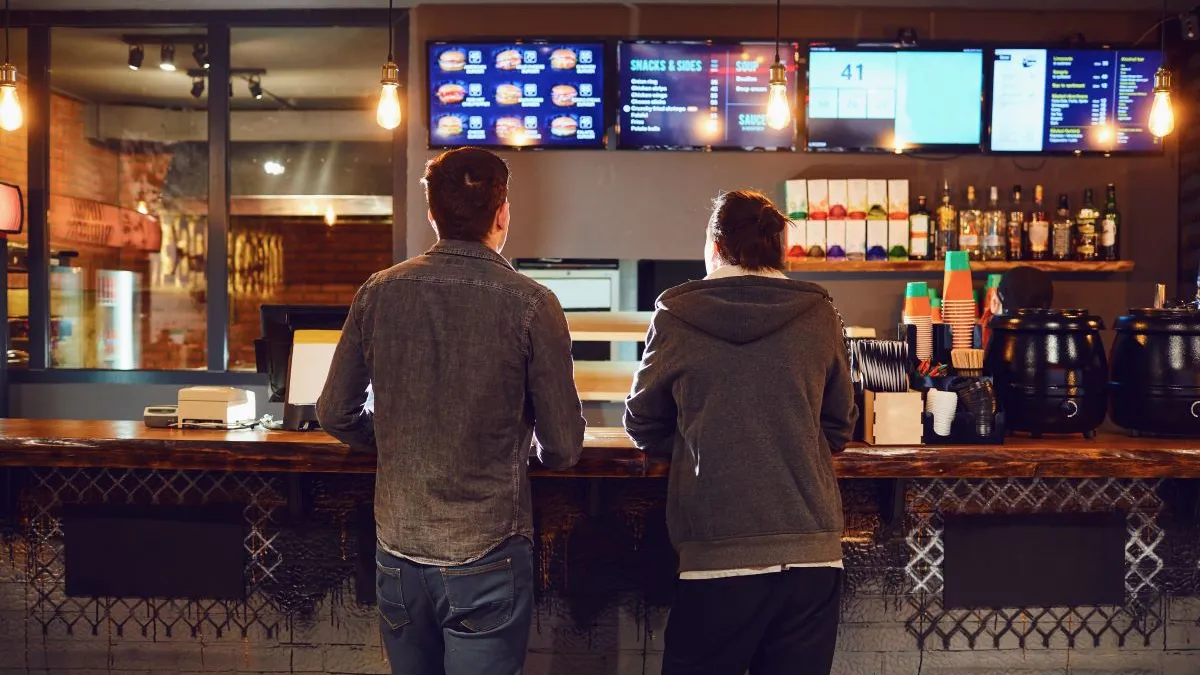 An image of two men standing at a counter ordering food.