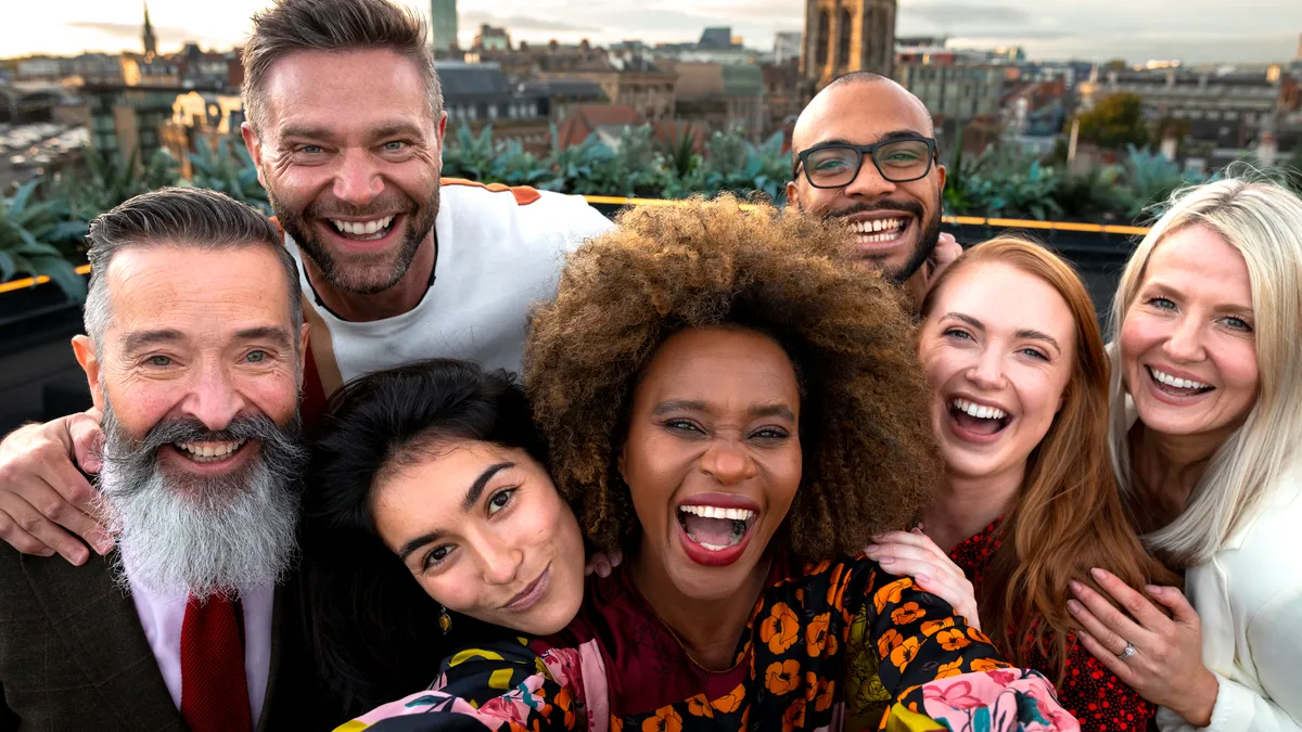 A wide selfie shot of a multiracial group of friends at a rooftop bar in Newcastle Upon Tyne. They are looking at the camera, smiling and laughing.