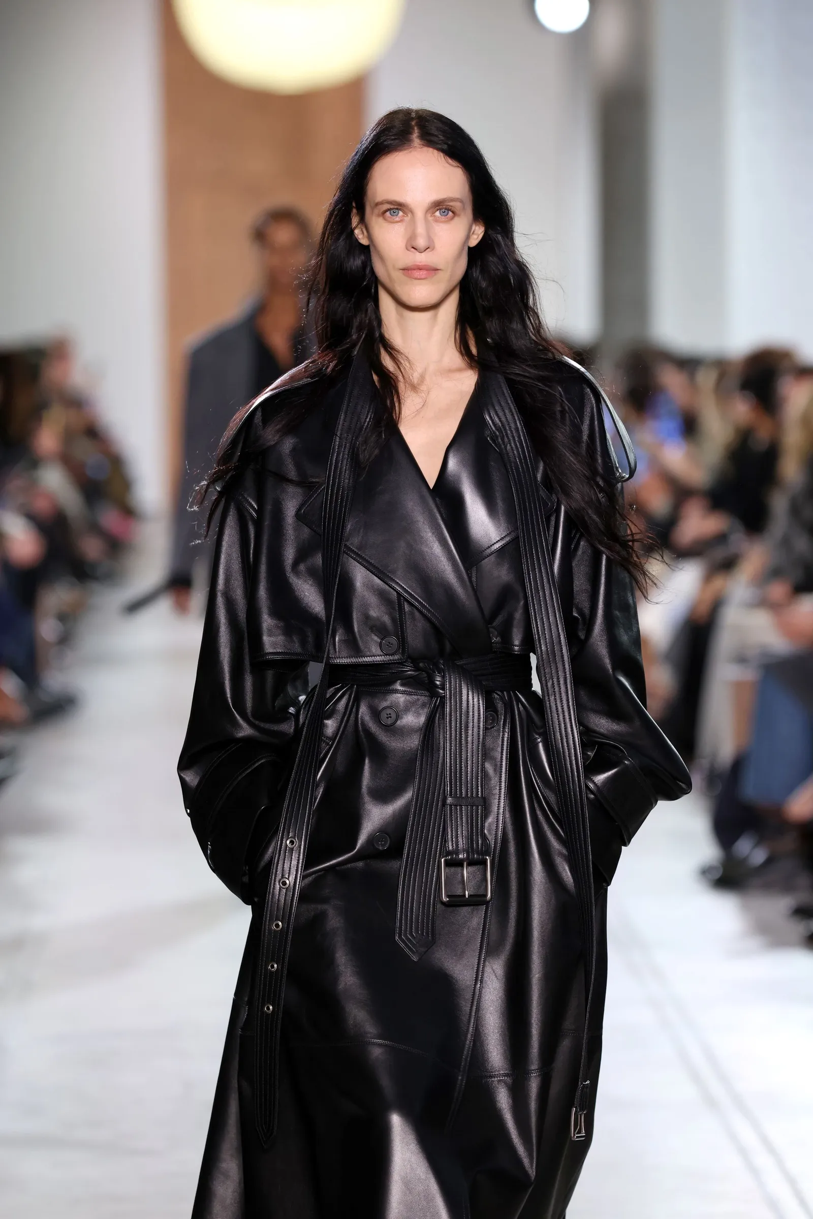 A model in a black leather coat walks down a runway.