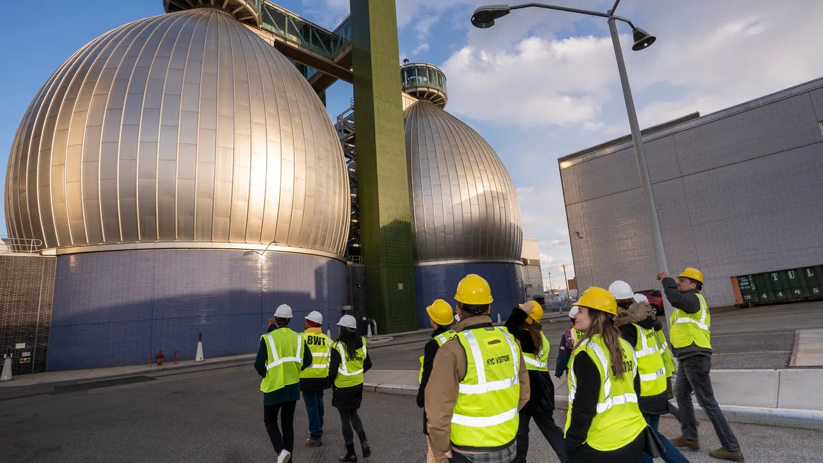 Workers tour a facility that features large, egg-shaped digesters visible in the background.