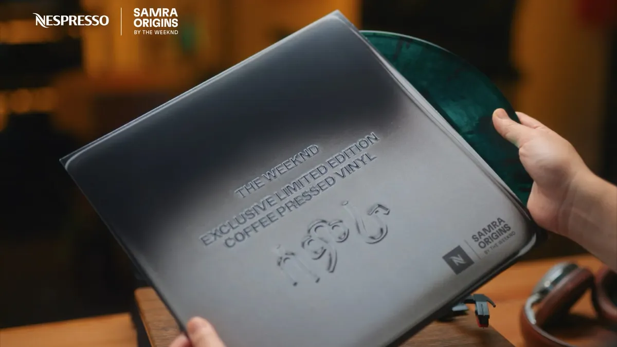 Hands hold the vinyl collaboration between The Weeknd and Nespresso, with the disc peaking out of the grey slip cover.