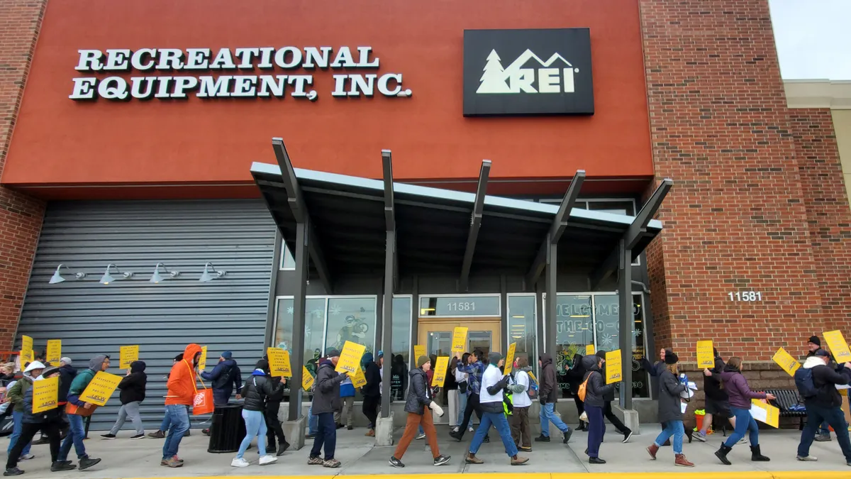 People with picket signs walk in front of store.