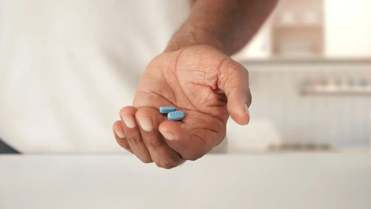 A person holds two blue drug tablets in their left hand.