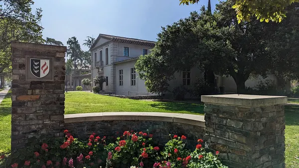 Stone wall in foreground with stucco Spanish-style building in background.