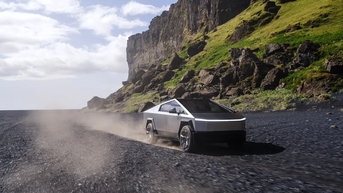 The 2024 Tesla Cybertruck outdoors with mountains and greenery in the background.