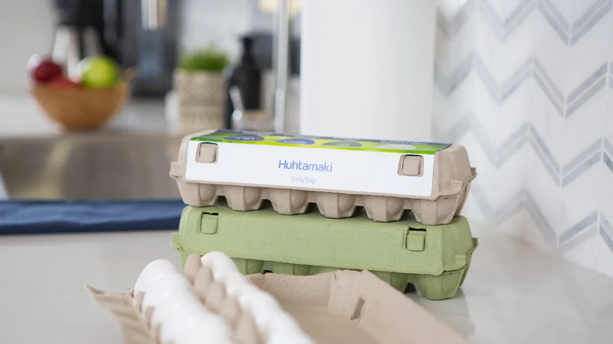 Two Huhtamaki fiber egg cartons stacked on top of each other, with another open carton in the foreground, on a kitchen counter.