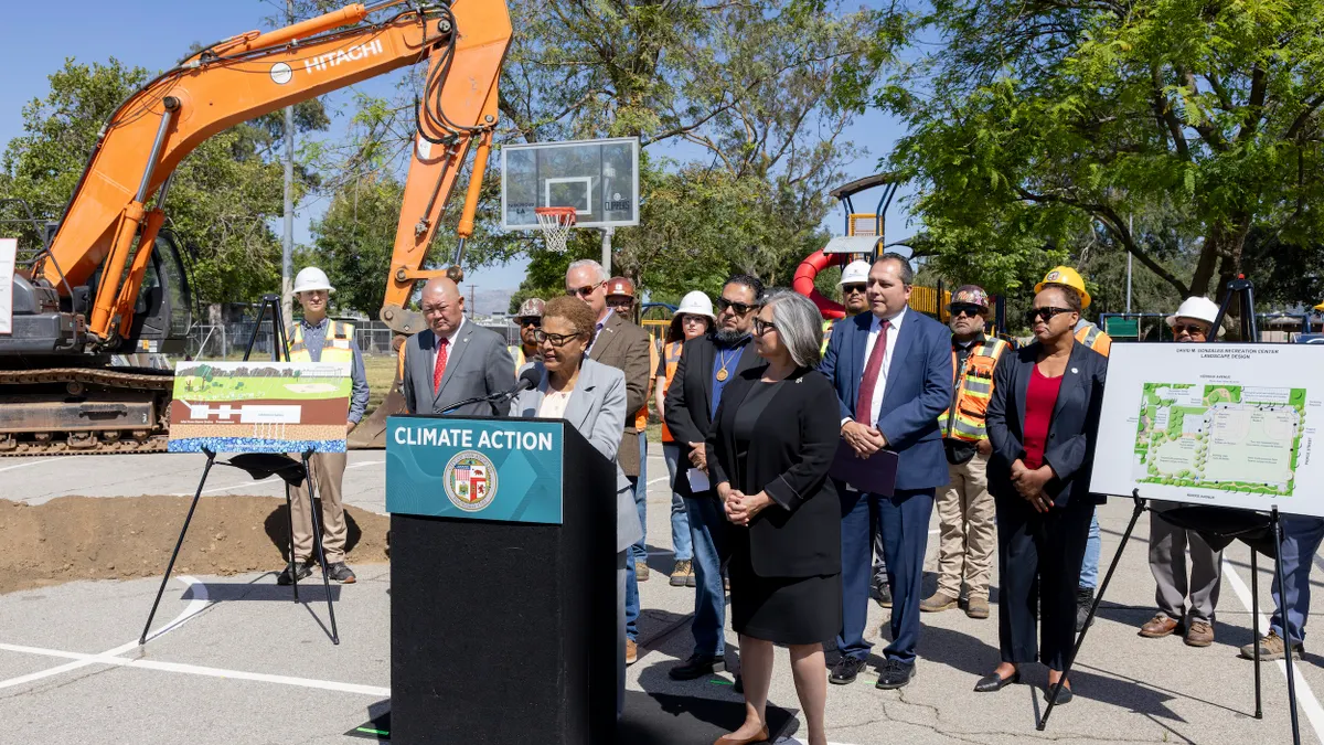 A person speaks at a podium surrounded by people and construction equipment.