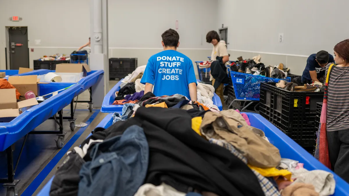 A Goodwill employee wearing a shirt that says "Donate Stuff Create Jobs" moves a bin of used clothing