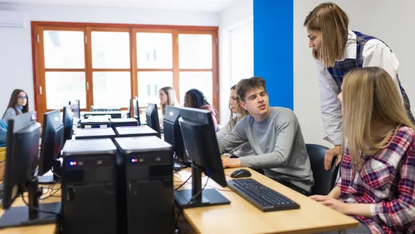 Students work on computers as a teacher looks over their shoulder