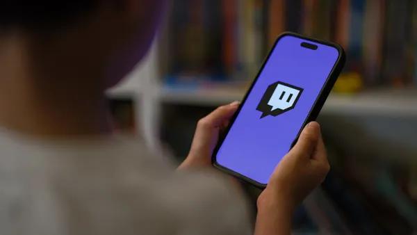 A young person holds a mobile device with the Twitch logo on it