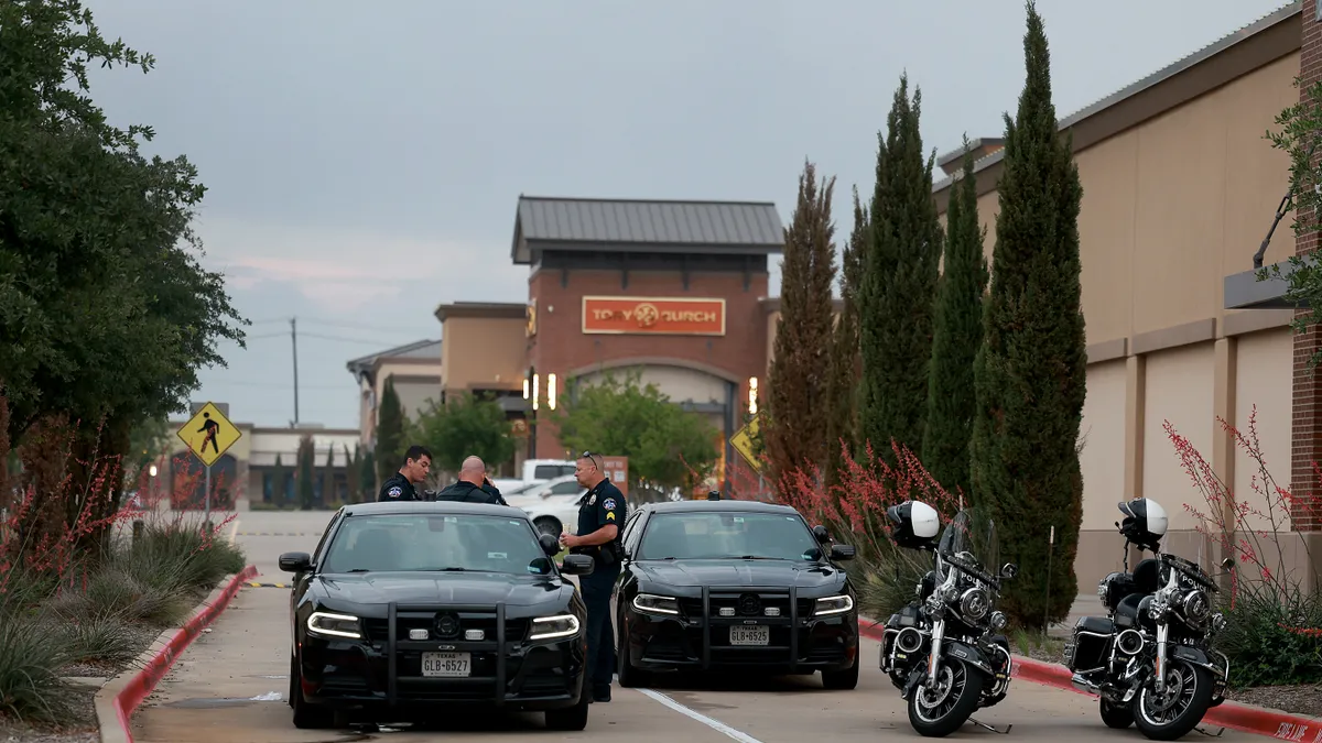 Police in uniform, police cars and police motorcycles block a mall entrance.