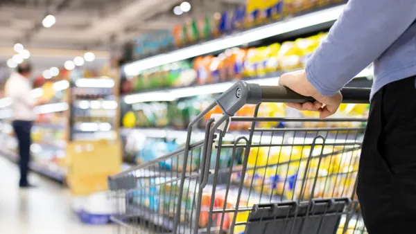 A person's hand is seen pushing a grocery cart in a store.