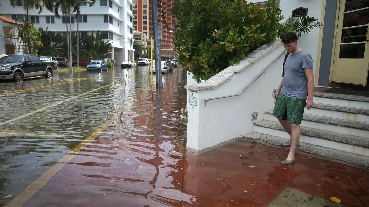 A person walking down stairs into the street is ankle deep in floodwater.