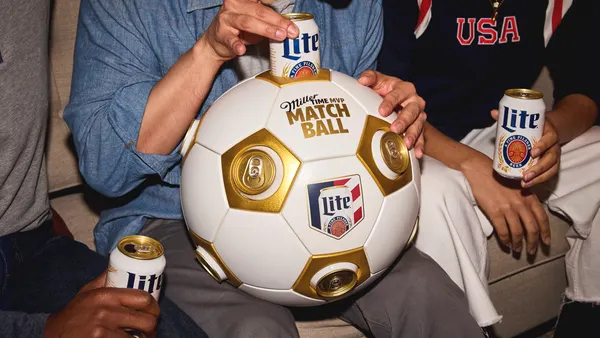 Three people sit on a sofa, heads not visible. All three hold Miller Lite's, with the person in the center holding the matchball.