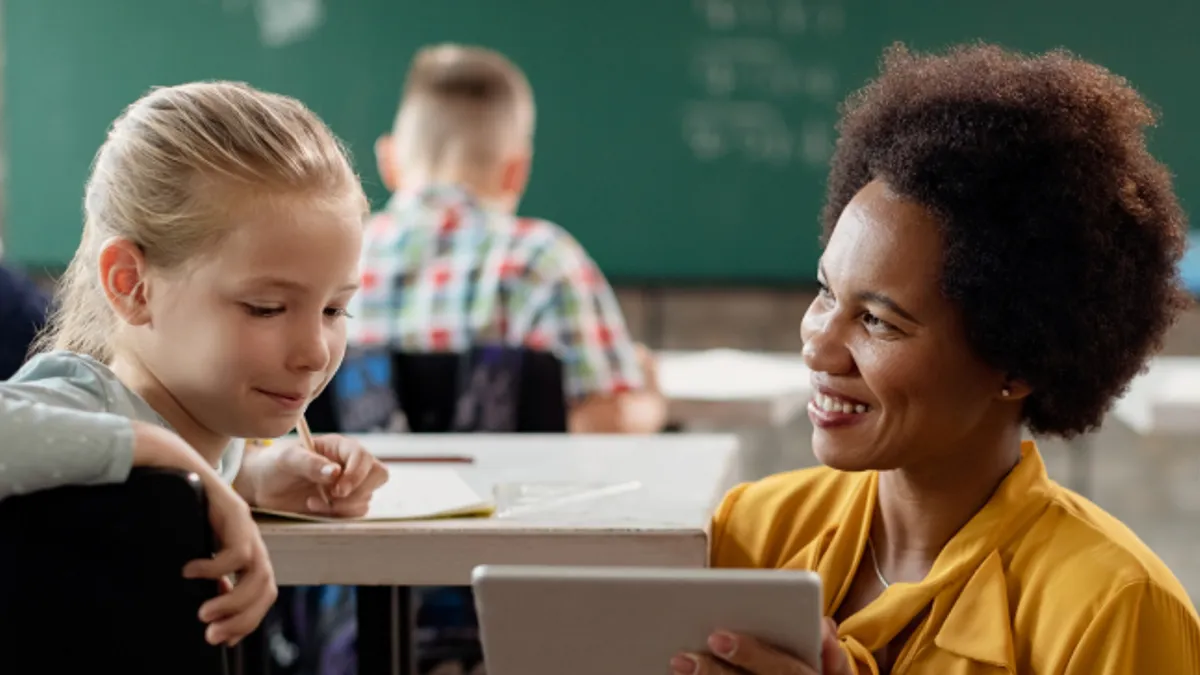 Happy teacher and schoolgirl using digital tablet in the classroom.