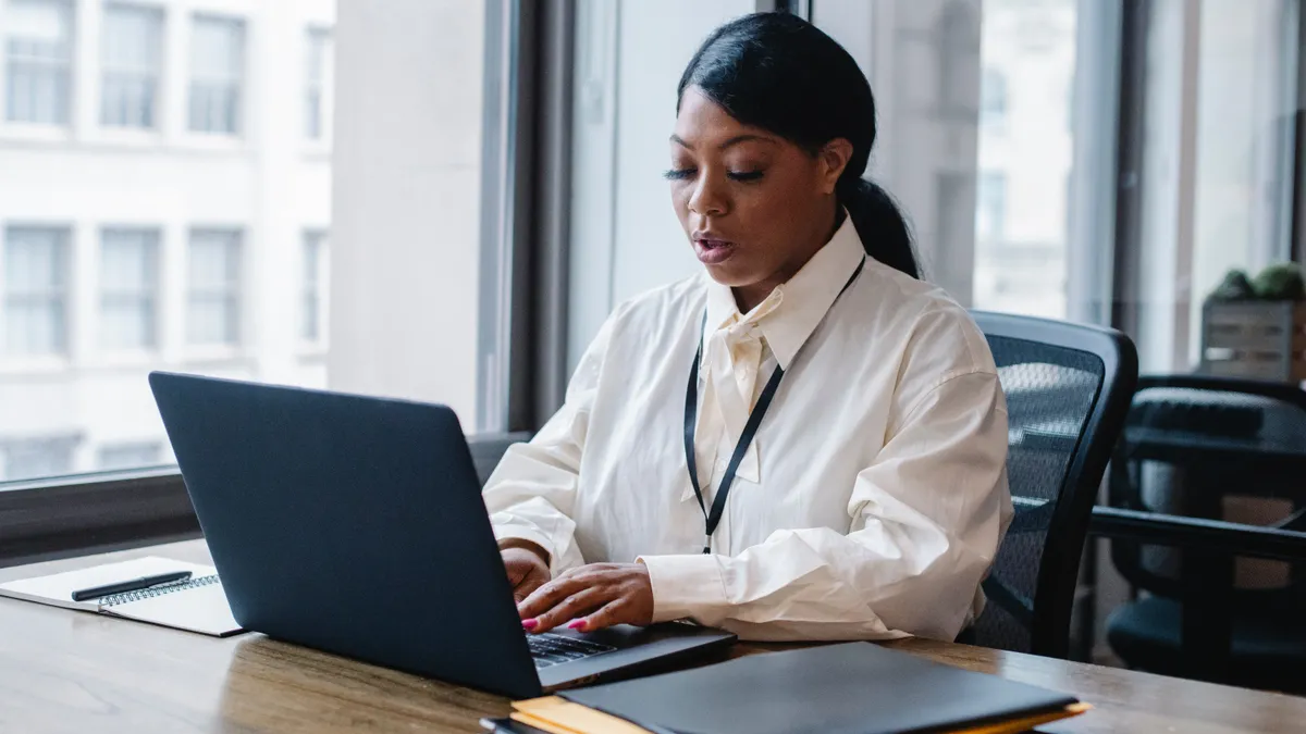 A Black person types on a laptop in the office