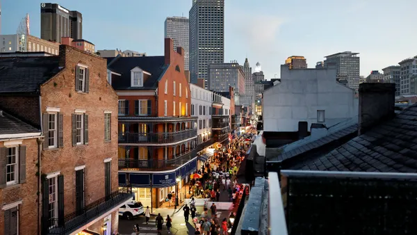 A mixture of historic and newer buildings fill a downtown district, as people walk along the street.