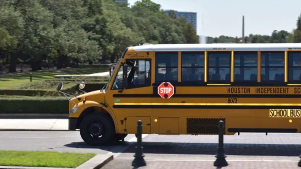 A yellow school bus drives along a street next to a park.