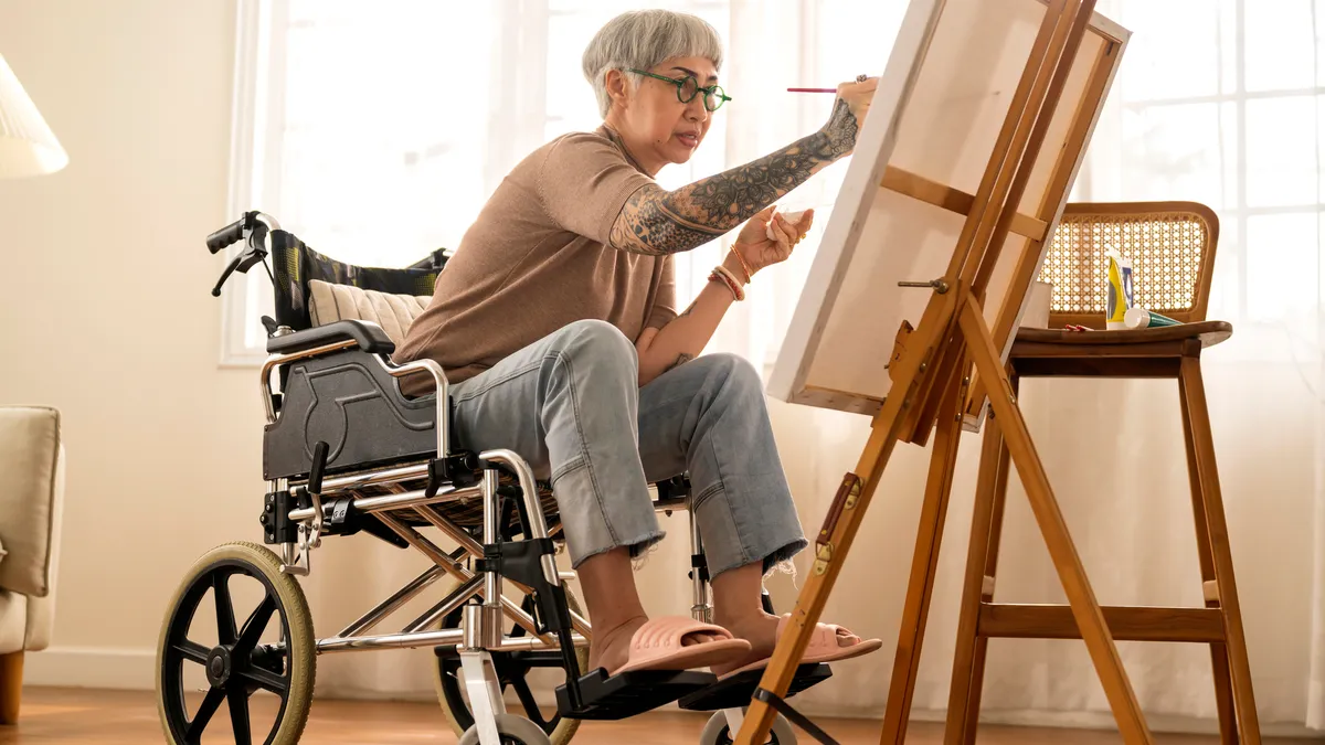 A person with tattoos in a wheelchair paints on a canvas