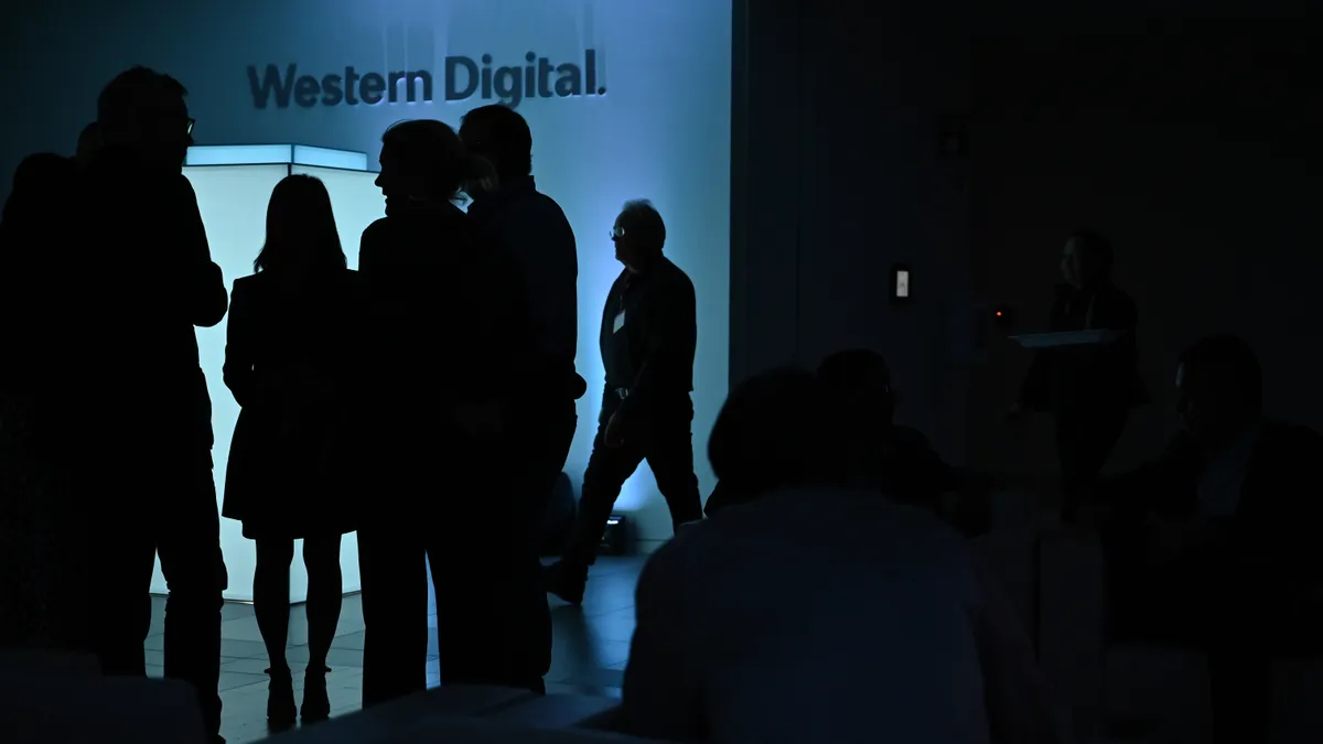 A group of people in shadow in front of a glowing square with a sign for Western Digital