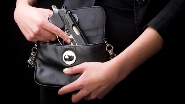 Close-up view of hands of a person putting a handgun into a black purse.