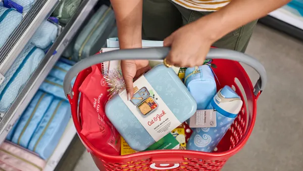A person holds a shopping basket full of items.