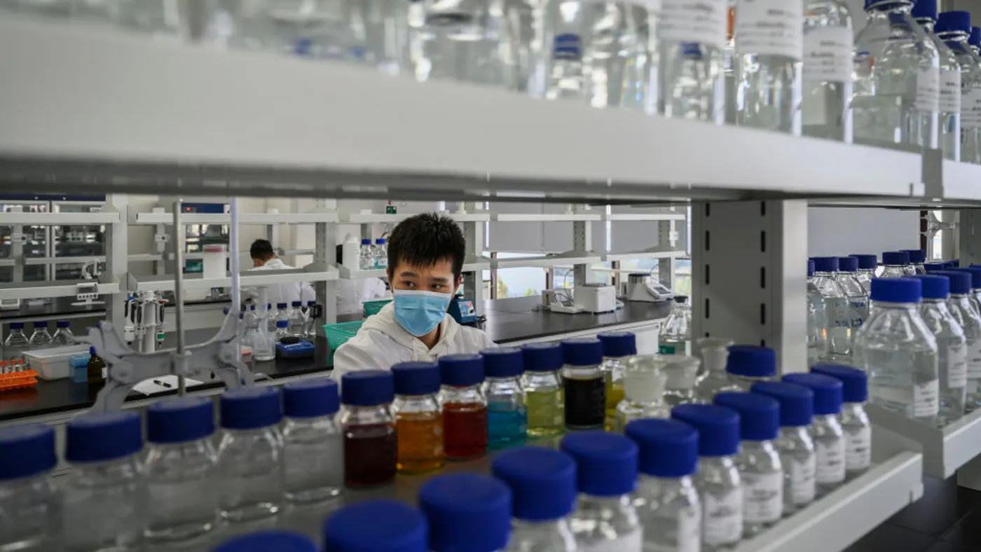 A technician wearing a blue mask works in a laboratory.