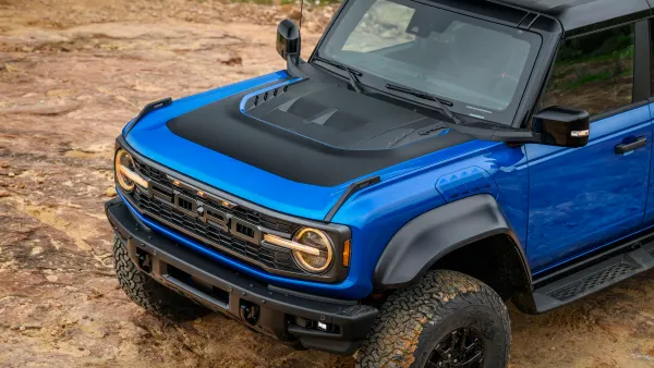 A view of the front half and hood of blue 2024 Ford Bronco Raptor from above with Black Appearance Package on a rocky trail outdoors.