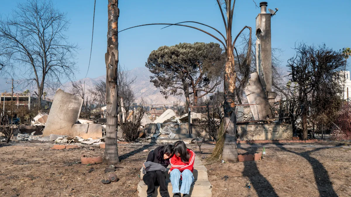 Two sisters lean on each other as they sit on the front steps of their home, which is now in rubble from the Southern California wildfires.