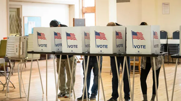 Four voting booths are lined up, filled with people.