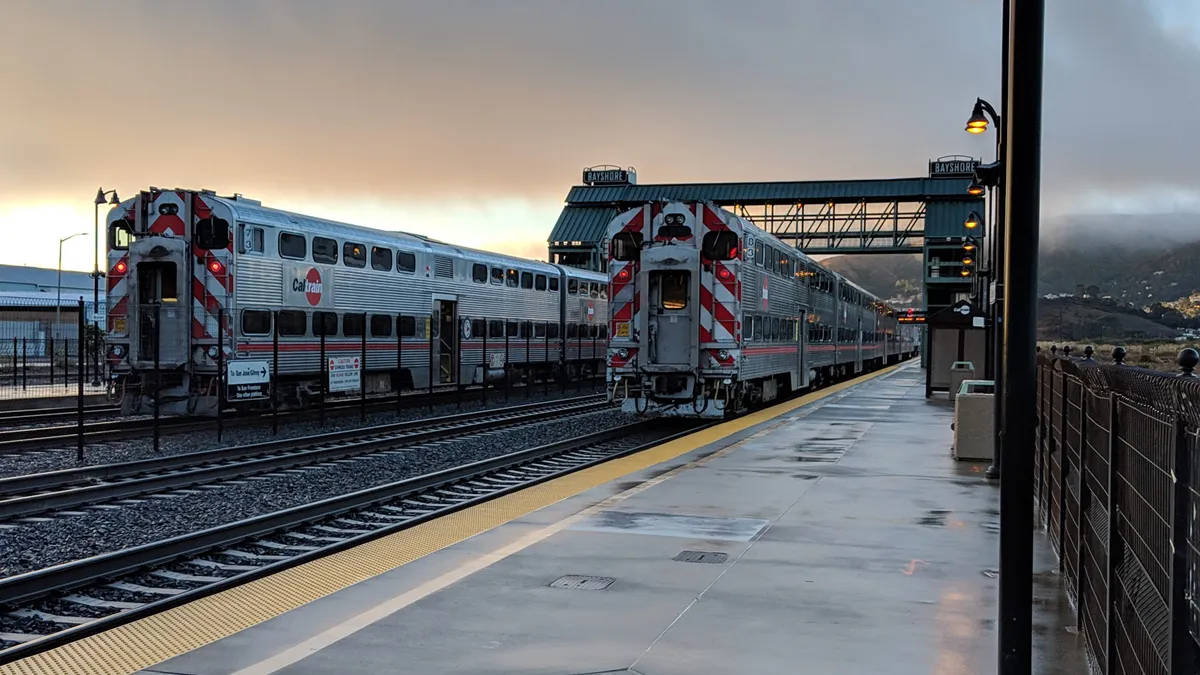 Two double-deck silver passenger trains are at a station in Northern California on a gray, wet day.