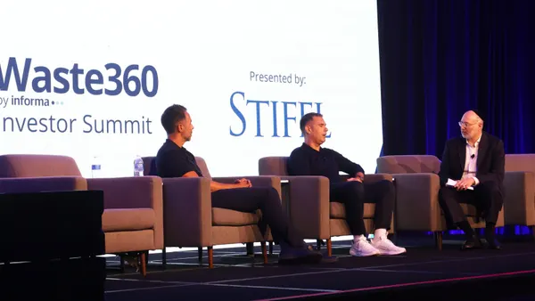 Three men sit on a stage. Behind them is a backdrop that reads "Waste 360 by Informa Investor Summit. Presented by Stifel."
